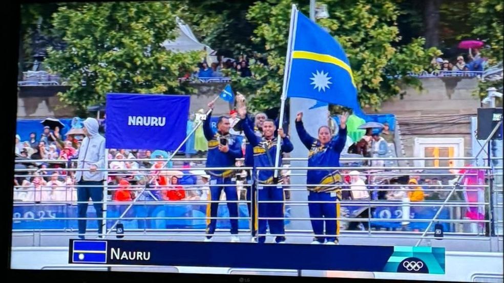 TV still of the Nauru team waving the national flag on a boat at the Paris 2024 opening ceremony